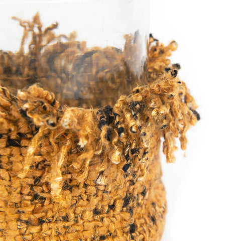 Close-up of a glass edge wrapped in a textured, knitted cotton material. The fabric is frayed at the top, with brown and black tones providing a rustic appearance.