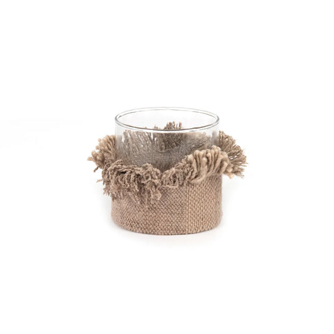 A clear glass container is wrapped with a textured beige and brown woven holder, reminiscent of hand-knitted artistry, featuring fringed edges that give it a rustic and handcrafted appearance. Perfect as an elegant addition to your candle holders collection, this holder covers the lower half of the glass.