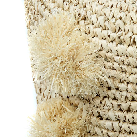 Close-up of a woven straw basket with two cream-colored tassels, exuding a breezy summer vibe. The natural, fibrous texture complements teak wood accents beautifully.