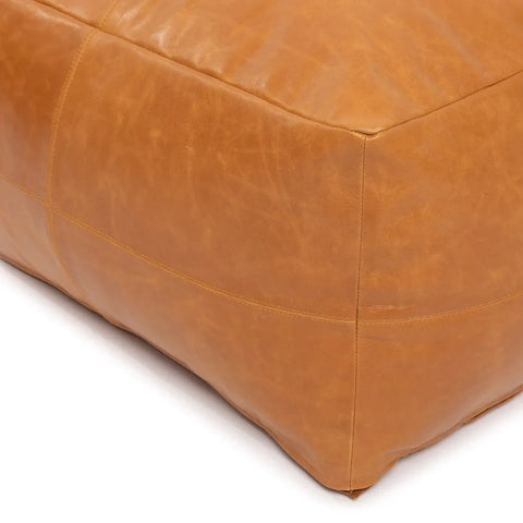 Close-up of a tan leather ottoman corner with visible stitching and a smooth texture. The nappa leather appears slightly worn, adding a touch of rustic elegance to this luxury accessory.