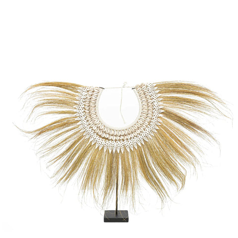 A decorative collar with long brown tassels radiates from a round base, where hand-placed shells form intricate white patterns. This bohemian beauty sits elegantly on a black stand against a white background.