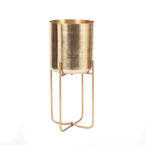 A tall, brass planter with a cylindrical pot on a minimalist stand featuring four legs. The design is sleek and modern, with a shiny finish that reflects light beautifully, perfect for an elegant indoor space against the plain white background.