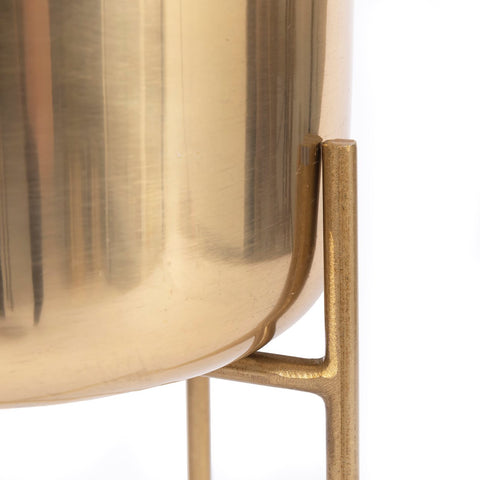 Close-up of a shiny brass planter perfect for any indoor space, supported by a metal stand with a sleek, modern design. The planter's surface shows some light scratches, and the stand boasts a minimalist, geometric style against a crisp white background.